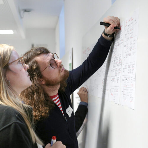 Zwei Personen Die Auf Ein Whiteboard Schauen. Eine Person Schreibt Etwas.